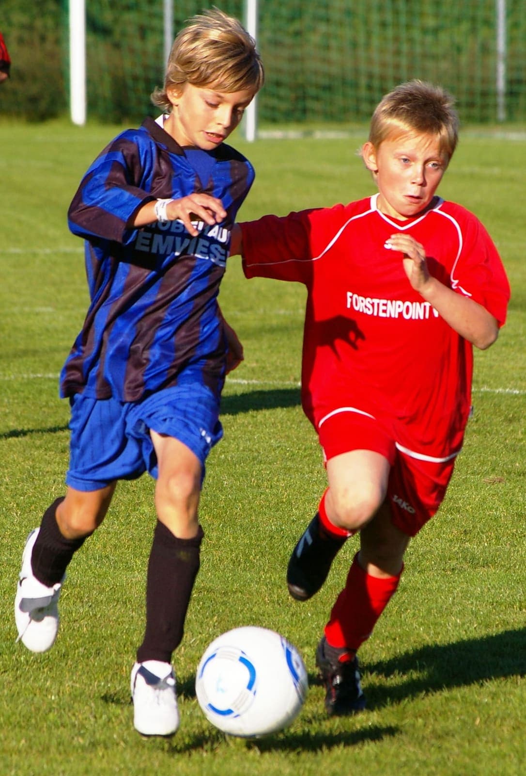 Two young footballers competing for the ball on a grass pitch