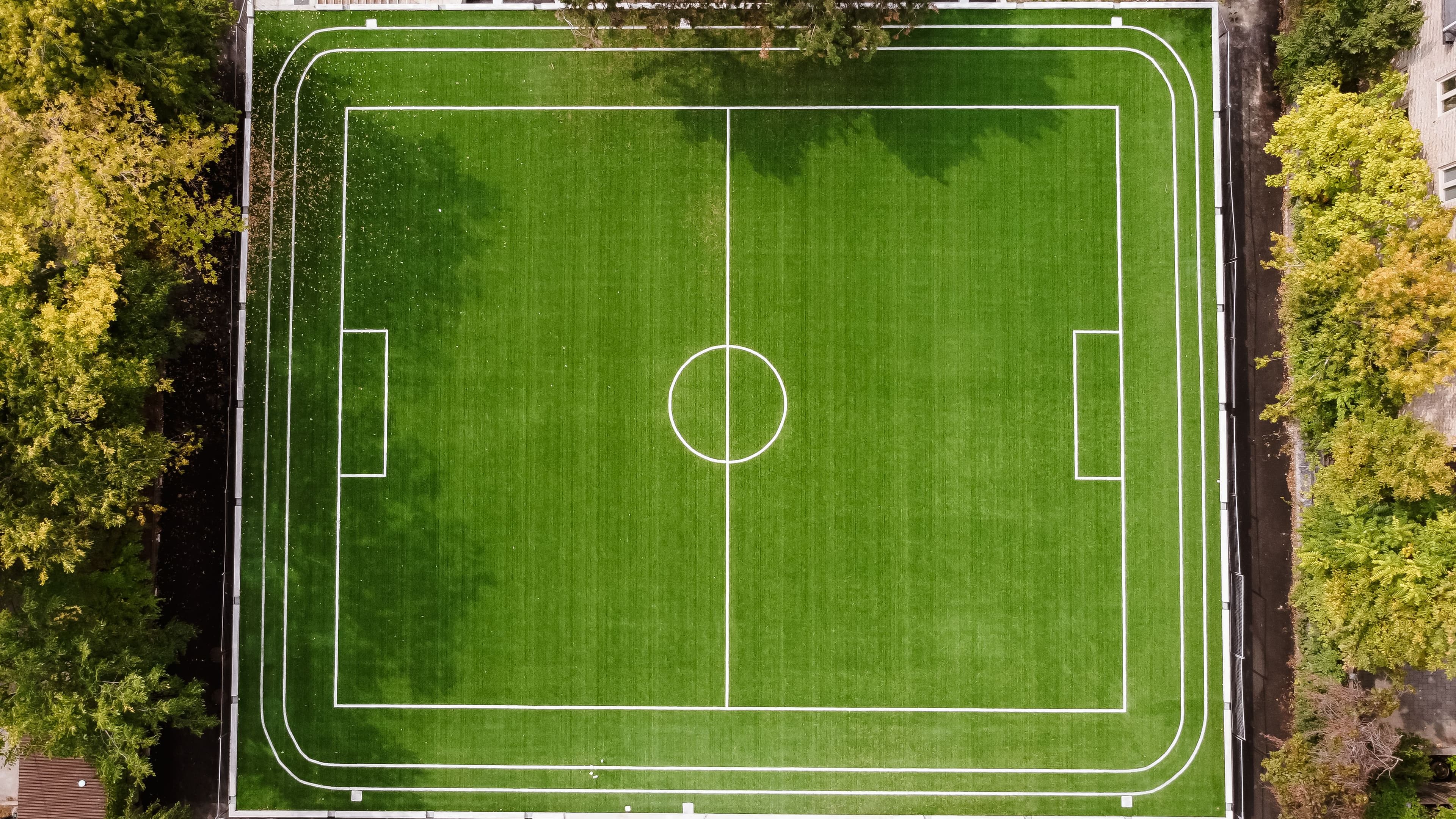Top‑down view of green football field surrounded by trees