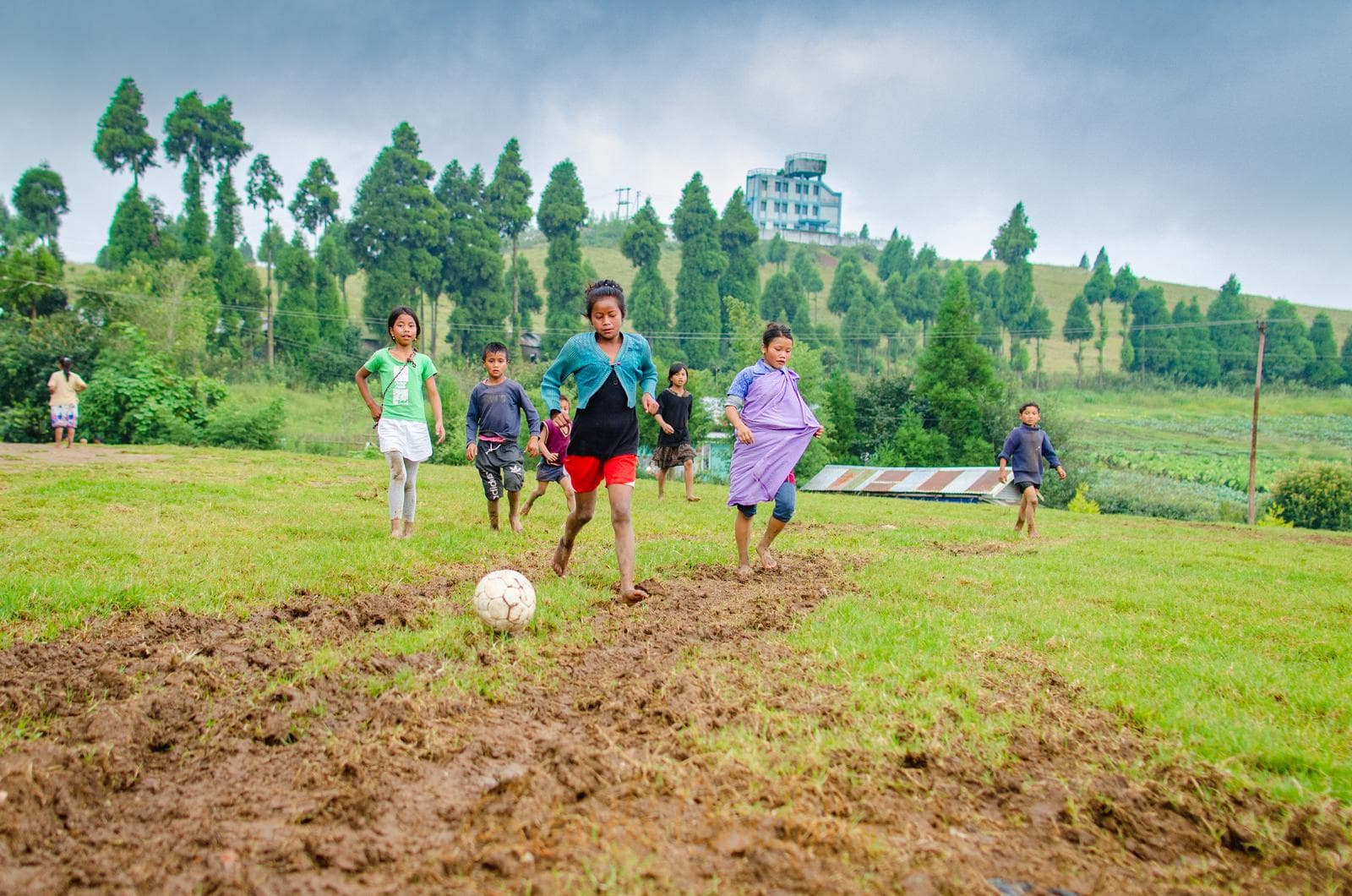 Khasi girls play football on a hillside field in Meghalaya, India, with the ball in front of them