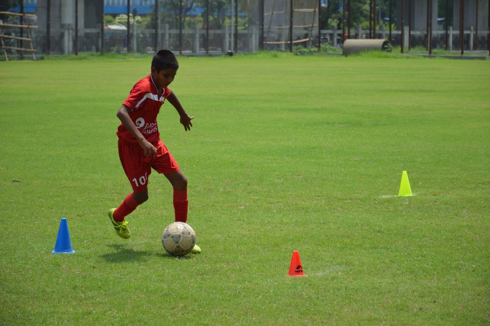 Under-14 boy in a red kit dribbles a football through cones during grassroots training in Kolkata