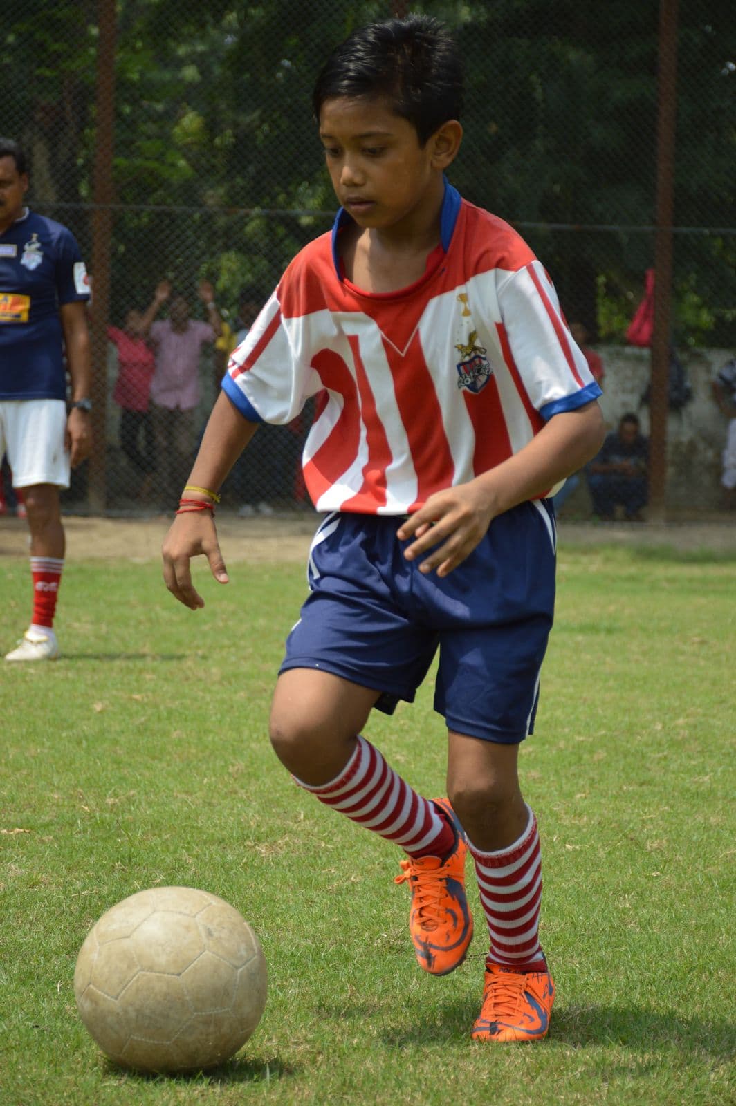Young footballer in a red-and-white striped kit dribbles a ball during the ATK grassroots programme in Kolkata