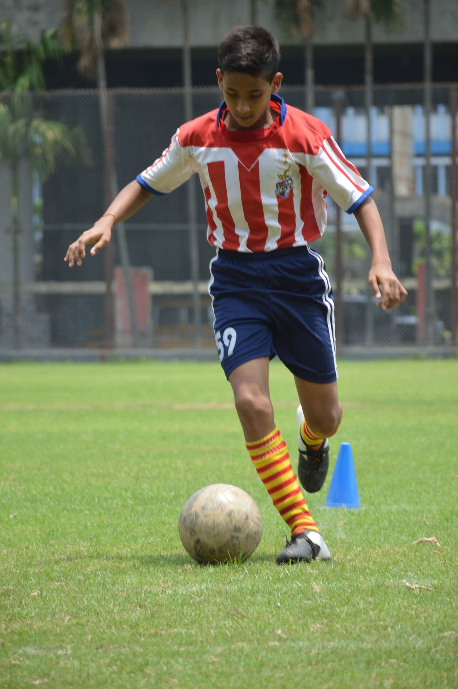 Young footballer in a red-and-white striped kit dribbles a ball at an under-14 session in Kolkata