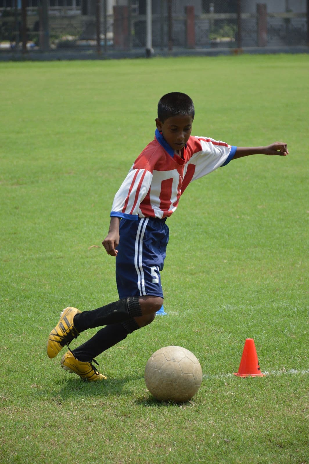 Young footballer in a red-and-white kit kicks a ball during an ATK grassroots dribble test in Kolkata