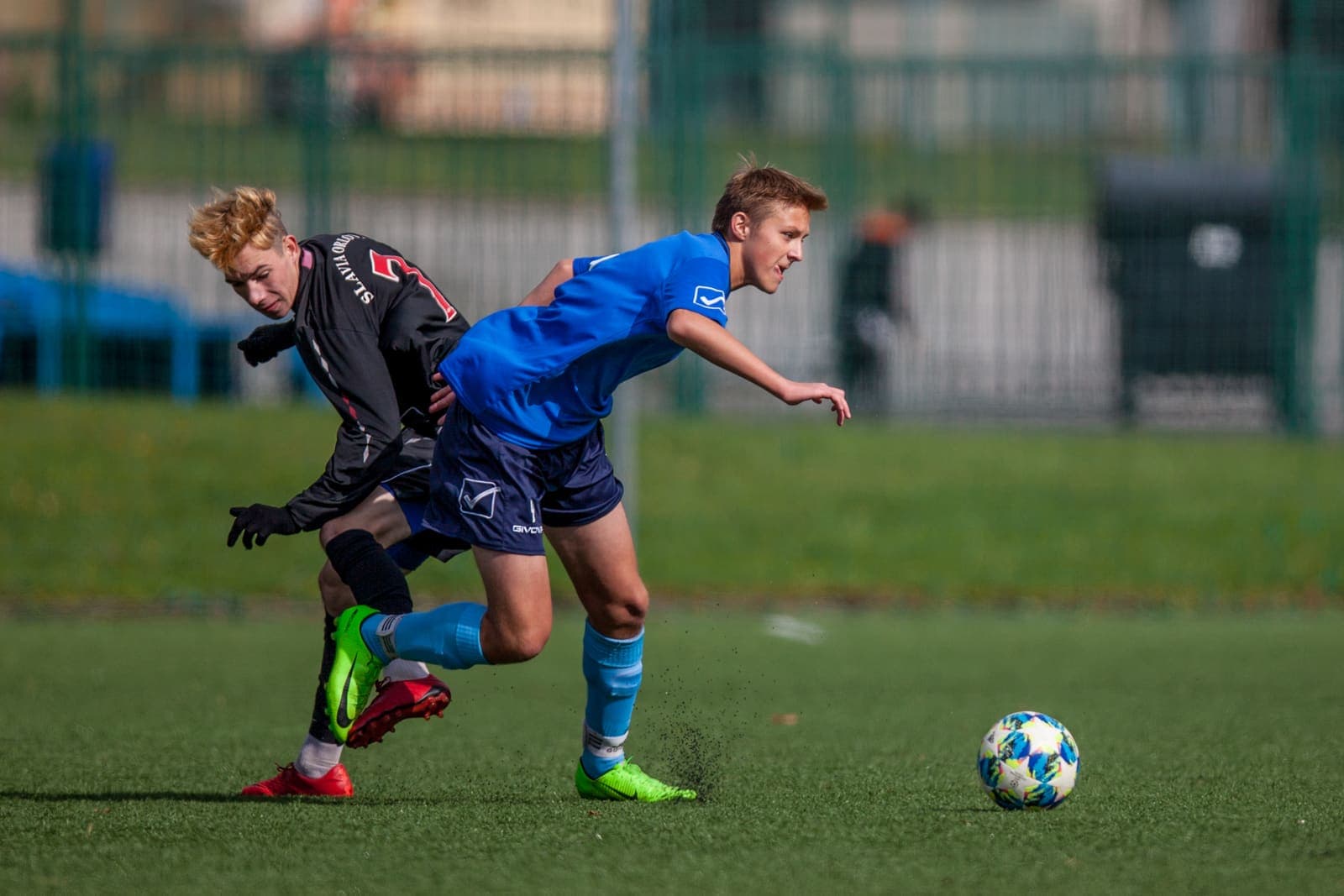 Two youth footballers contesting the ball on a grass pitch